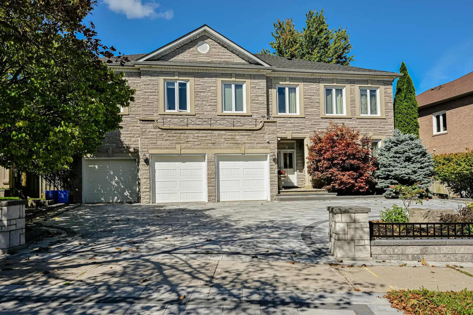 Finished grey interlock driveway with stone pillar walls at a stone home's two-car garage