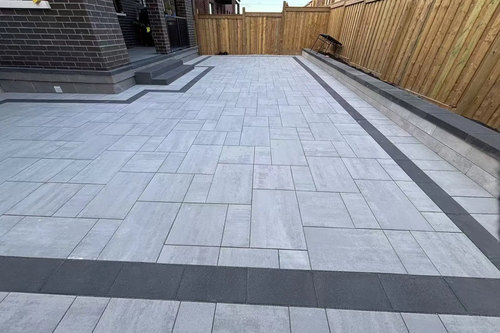 Grey interlock driveway -- large-format pavers, dark charcoal curved border, GTA brick home with double garage