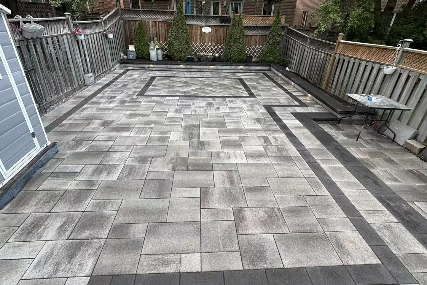 Grey interlock driveway -- large-format pavers, dark charcoal curved border, GTA brick home with double garage